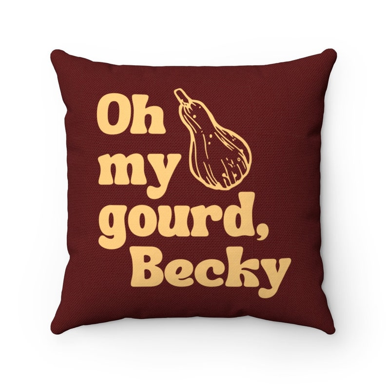 May include: A square throw cushion in a deep maroon colour featuring a light yellow graphic of a butternut squash and the text "Oh my gourd, Becky" printed in a bold, rounded font across the front of the fabric surface.