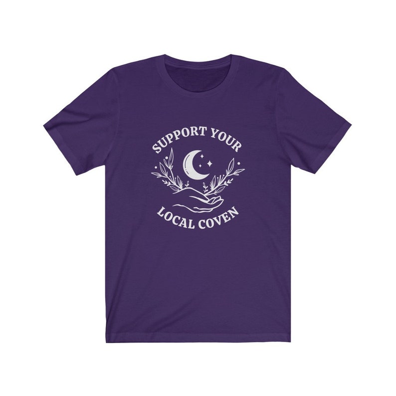 May include: Purple short-sleeved t-shirt with a white graphic design that says "Support Your Local Coven" with a crescent moon and stars in the design.