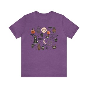 May include: Purple t-shirt with a vintage Halloween design featuring cats, owls, pumpkins, skulls, bats, and the text "Trick or Treat" and "Boo!"