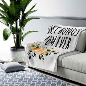 May include: White throw blanket with a floral design and the text "Best Donuts Ever" in black.