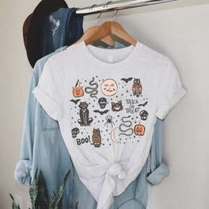 May include: A gray t-shirt with a Halloween-themed design featuring a black cat, owl, pumpkins, bats, skulls, snakes, and stars. The text "Trick or Treat" and "Boo!" are also included in the design.