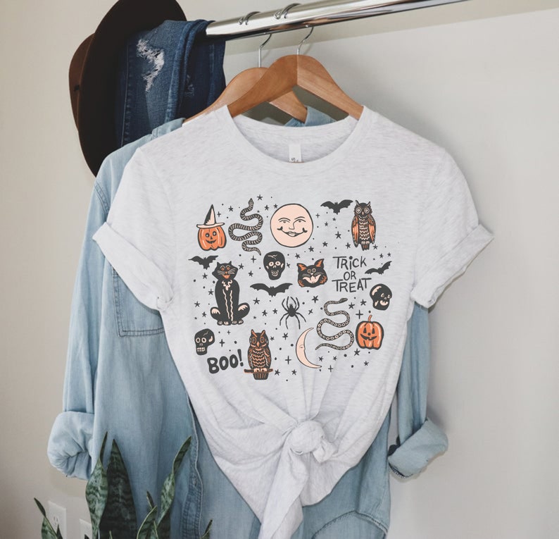 May include: A gray t-shirt with a Halloween-themed design featuring a black cat, owl, pumpkins, bats, skulls, snakes, and stars. The text "Trick or Treat" and "Boo!" are also included in the design.