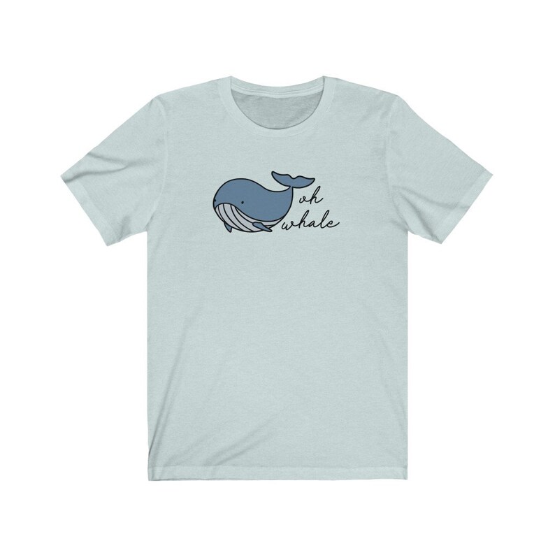 以下が含まれることがあります： 薄い青色のTシャツに、漫画のクジラと黒い文字で「oh whale」と書かれている