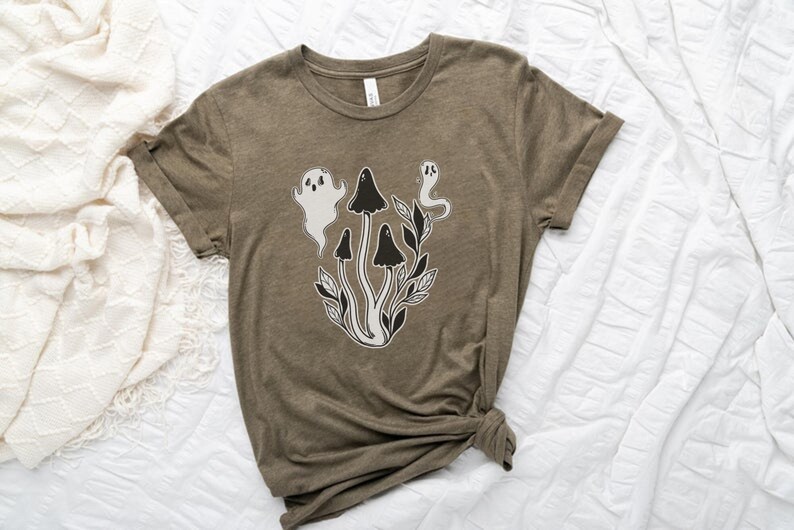 Puede incluir: Una camiseta verde con un gr&aacute;fico blanco y negro de setas y fantasmas. El gr&aacute;fico est&aacute; centrado en la camiseta.