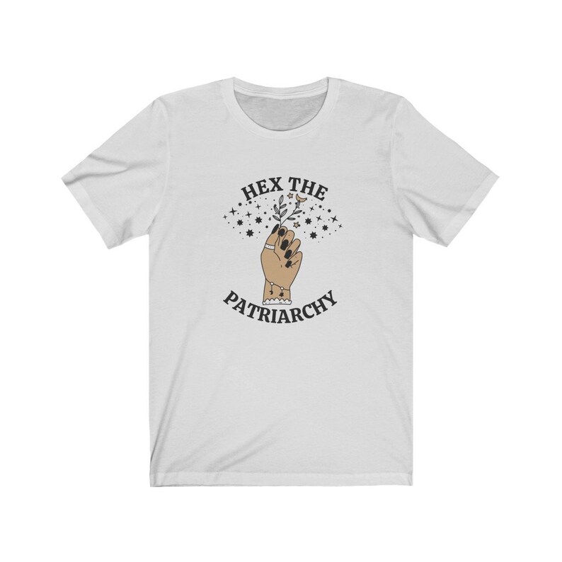 May include: White t-shirt with a graphic design featuring a raised hand holding a sprig of leaves and stars. The text "HEX THE PATRIARCHY" is arched above and below the hand in a circular design.