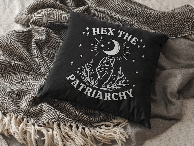 K&ouml;nnte beinhalten: Schwarzes Kissen mit wei&szlig;em Text, der "Hex the Patriarchy" lautet, und einer Grafik einer Hand, die einen Halbmond mit Sternen h&auml;lt.