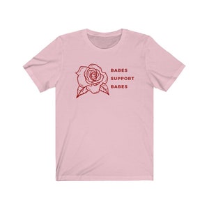 May include: Pink short-sleeved t-shirt with a red rose graphic and the text "BABES SUPPORT BABES".