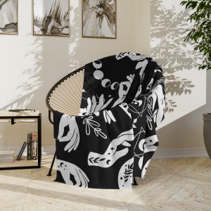 May include: Black and white throw blanket with a repeating pattern of hands, moons, stars, and leaves. The blanket is draped over a chair.