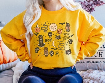 May include: A mustard yellow crewneck sweatshirt featuring a black graphic print of Halloween-themed icons including a cat, owls, pumpkins, skulls, snakes, bats, a spider, a crescent moon, a sun face, and the text BOO! and TRICK OR TREAT.