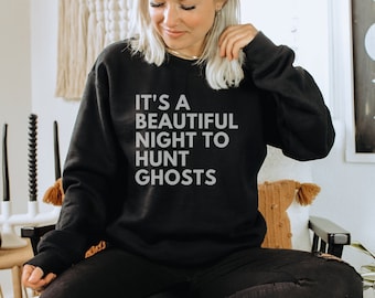 Könnte beinhalten: Ein schwarzer Pullover mit dem Text "It's a beautiful night to hunt ghosts" in weißen Buchstaben.