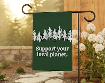 Puede incluir: Una bandera de jardín verde con una silueta blanca de una fila de pinos y el texto "Apoya tu planeta local."
