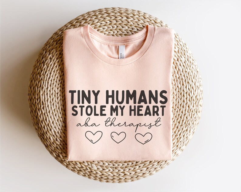May include: A pink t-shirt with the text "Tiny Humans Stole My Heart aka therapist" and three small hearts.