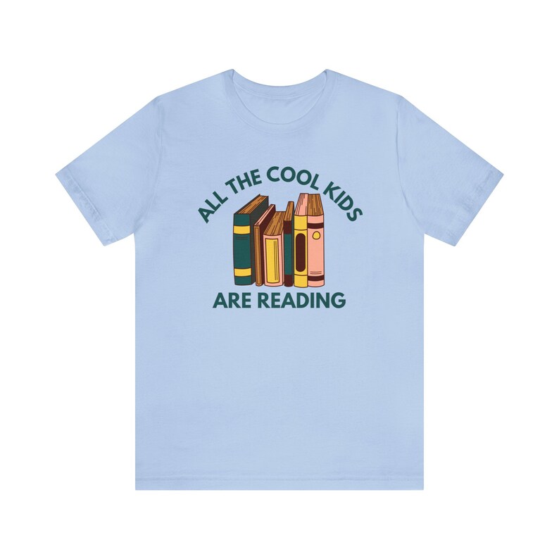 Puede incluir: Camiseta azul claro con el texto "All the cool kids are reading" y una pila de libros coloridos.