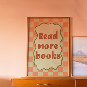 May include: A wooden dresser with four drawers and brass pulls. Above the dresser is a framed poster with a pink and white checkered background and the text "Read more books" in a green and orange font.