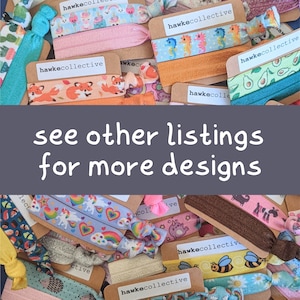 May include: A collection of colorful hair ties with various patterns, including unicorns, avocados, bees, and foxes. The hair ties are packaged on brown cards with the text "hawkecollective" printed on them. The text "see other listings for more designs" is printed on a gray background.