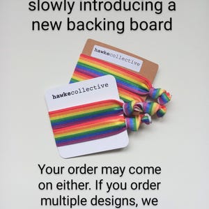 May include: Two rainbow elastic hair ties with the text "hawkecollective" on the backing cards. The text "Please note: we are slowly introducing a new backing board. Your order may come on either. If you order multiple designs, we will try to match the backing boards." is printed below the hair ties.