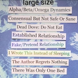 Op de afbeelding: Een verzameling rechthoekige papieren stroken met verschillende zinnen erop gedrukt, waaronder "Alpha/Beta/Omega Dynamics" en "I Wrote This Instead of Sleeping". De achtergrond is een blauw-wit patroon.