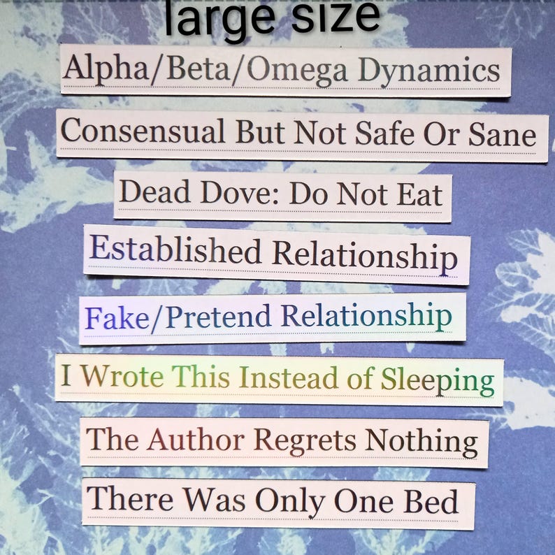 Op de afbeelding: Een verzameling rechthoekige papieren stroken met verschillende zinnen erop gedrukt, waaronder "Alpha/Beta/Omega Dynamics" en "I Wrote This Instead of Sleeping". De achtergrond is een blauw-wit patroon.