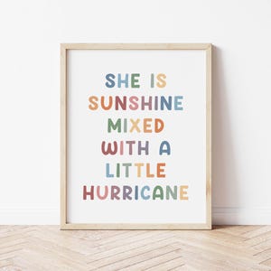 Puede incluir: Una impresión enmarcada con el texto "She is sunshine mixed with a little hurricane" en letras de colores sobre un fondo blanco.