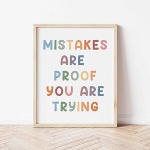 Op de afbeelding: Een ingelijst print met de tekst "Mistakes are proof you are trying" in kleurrijke letters op een witte achtergrond.