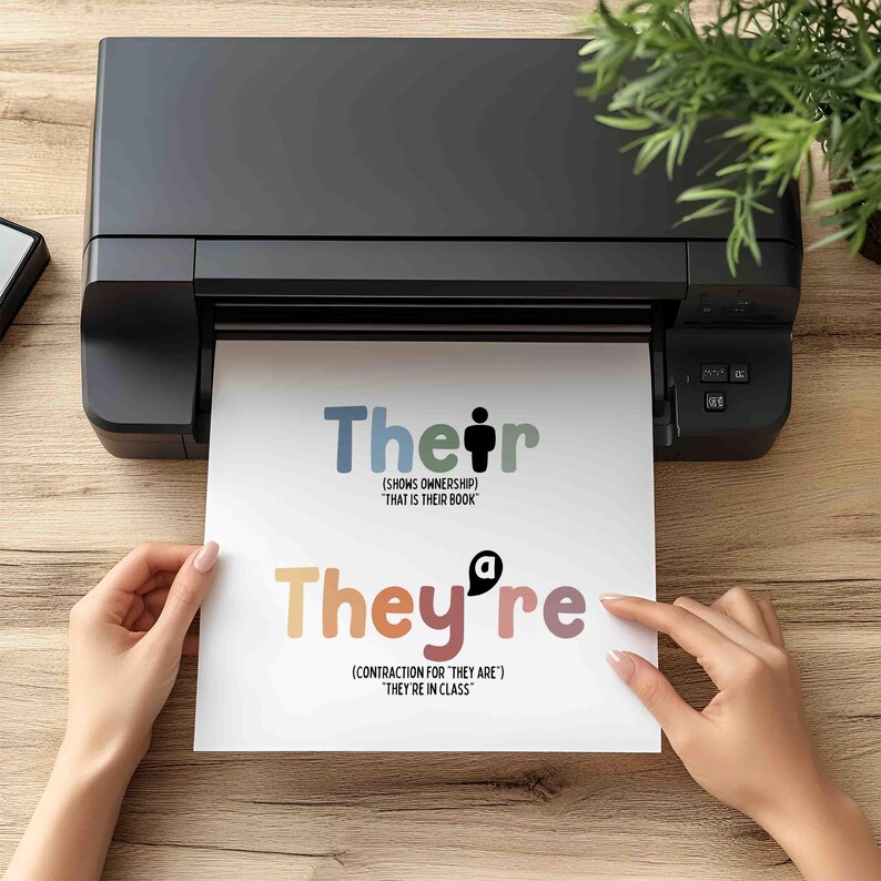 May include: A black printer printing a white sheet of paper with the words "Their" and "They're" in colorful text. The text explains the difference between the words. The paper is on a wooden surface.