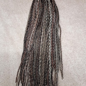 May include: A collection of long, individual synthetic hair braids featuring a multi-tonal color palette of dark brown, medium brown, and light ash blonde strands woven together to create a blended, textured appearance throughout the length.