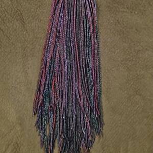 May include: A collection of synthetic hair extensions in a mix of colours, including purple, red, and teal. The hair is styled into many small braids, giving a textured and lively look. The braids are closely woven and hang down, displaying the colour blend.