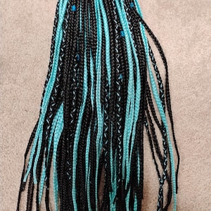 May include: Black and turquoise braided hair extensions. The braids are a mix of black and turquoise strands, with a few small blue beads. The hair is styled in individual braids, suitable for various hairstyles.
