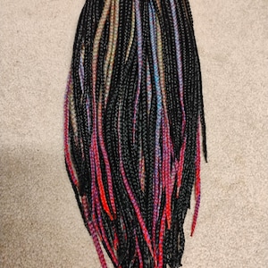 May include: A bundle of black synthetic hair braids with colorful highlights. The braids have streaks of red, pink, blue, and yellow. The braids are arranged in a vertical pattern against a neutral background.