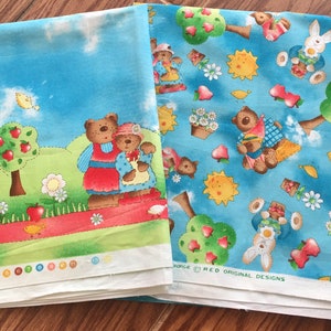 May include: Two pieces of blue fabric with a white background. One piece features a family of bears with red, yellow, and green accents. The other piece features a repeating pattern of bears, bunnies, and suns with red, yellow, and green accents. The text "RED ORIGINAL DESIGNS" is printed on the bottom of the fabric.