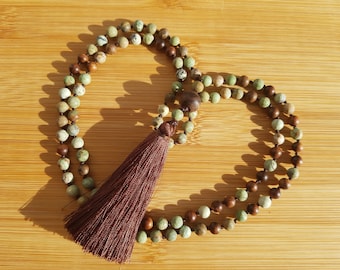 May include: A green and brown beaded mala necklace with a brown tassel. The necklace is made of natural stones and is approximately 108 beads long.