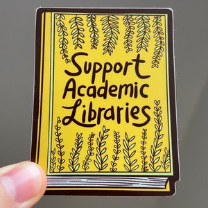Puede incluir: Una pegatina amarilla con un diseño de libro y el texto "Support Academic Libraries" en letras negras. El libro está decorado con hojas verdes.