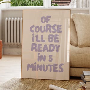 Peut inclure: Affiche encadrée avec le texte "OF COURSE I'LL BE READY IN 5 MINUTES" en lettres lavande. L'affiche est présentée dans un salon, appuyée contre un mur près d'une fenêtre et d'un canapé.