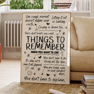 May include: A framed print with the words "THINGS TO REMEMBER WHEN YOU WANT TO CRY." The text is in black on a cream background, with decorative elements like hearts and stars. The print is displayed in a well-lit room.
