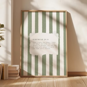 May include: A framed print with a light brown wooden frame. The print has a green and white striped background with a white paper overlay containing the text "JEREMIAH 29:11". The print is leaning against a wall.