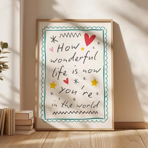 Pode incluir: Uma impressão artística emoldurada com as palavras "How wonderful life is now you're in the world". A obra de arte apresenta um fundo branco com texto manuscrito preto, corações vermelhos, estrelas amarelas e uma borda turquesa. A moldura é de cor castanho claro.