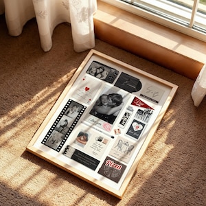May include: A framed collage featuring various photographs and mementos. The display includes black and white photos, playing cards, and text that reads "I love you", "Selfie!", and "Pizza". The frame is light-colored.
