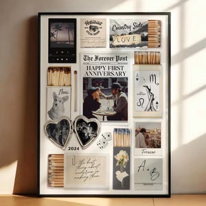 May include: A framed collage featuring various mementos. Includes a digital media player, restaurant sign, matchboxes, a newspaper with "HAPPY FIRST ANNIVERSARY", a dog portrait, heart-shaped locket, dice, and a photo with "Forever" text. The collage is in a black frame.