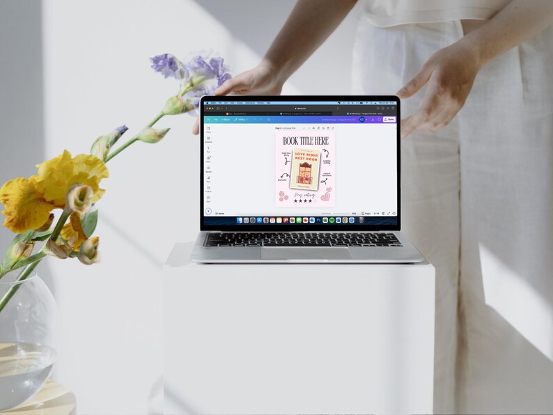 Pode incluir: Uma tela de laptop exibindo uma maquete de capa de livro com o texto "BOOK TITLE HERE" e um fundo rosa. A capa apresenta uma ilustra&ccedil;&atilde;o de desenho animado de uma pessoa com um livro e o texto "Little Words, Big Magic".