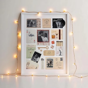 May include: A white framed collage featuring various vintage-style images and ephemera. Includes black and white photos, playing cards, a key, and ticket stubs. A string of warm white fairy lights surrounds the frame, creating a cozy aesthetic.