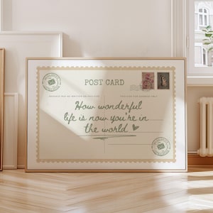 May include: A framed postcard print with a vintage aesthetic. The text reads "How wonderful life is now you're in the world." The design includes postage stamps and a postmark, evoking a sense of nostalgia and sentimentality.