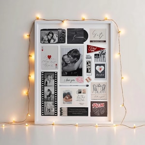 May include: A white framed collage featuring photos, cards, and decorative elements. Includes a photo of two people, a film strip, and the text "I love you" and "selfie!". Fairy lights surround the frame.