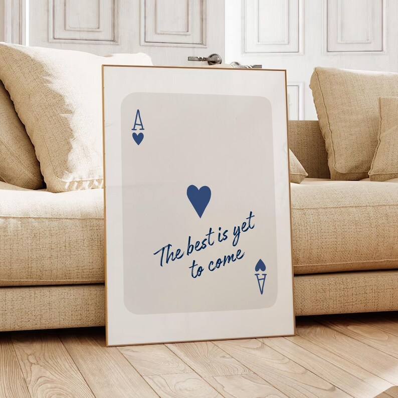 May include: Framed art print featuring a playing card design. The card is white with blue heart symbols and the text "The best is yet to come" in a cursive font. The frame is gold.