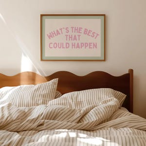 May include: A framed print with the text "WHAT'S THE BEST THAT COULD HAPPEN" in pink lettering. The print is above a bed with striped bedding and a wooden headboard. The room has a neutral color palette.