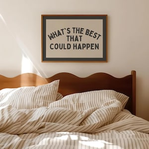 May include: A framed print with the text "WHAT'S THE BEST THAT COULD HAPPEN" in a black font. The print is above a bed with striped bedding and a wooden headboard. The room has a neutral color palette.