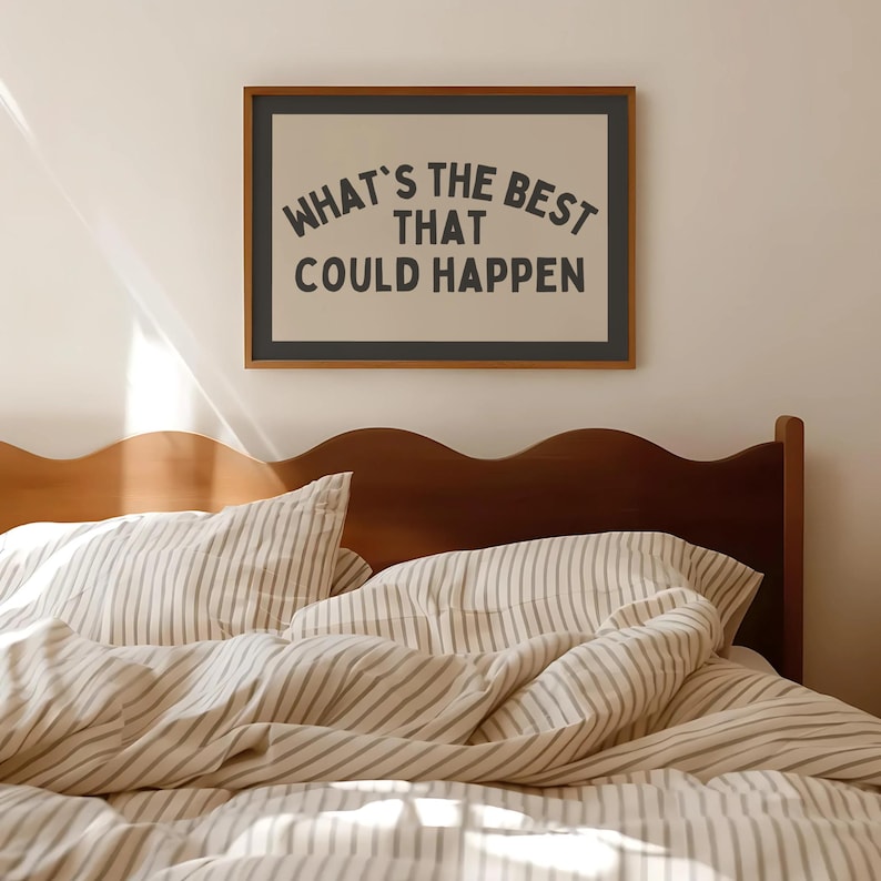 May include: A framed print with the text "WHAT'S THE BEST THAT COULD HAPPEN" in a black font. The print is above a bed with striped bedding and a wooden headboard. The room has a neutral color palette.