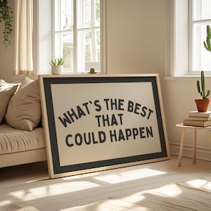 May include: A framed art print with the text "WHAT'S THE BEST THAT COULD HAPPEN" in black on a beige background. The frame is a light wood color with a black border. The print is leaning against a beige sofa in a well-lit room.