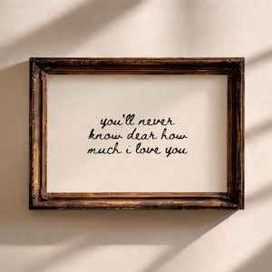 May include: A framed print featuring the handwritten text "you'll never know dear how much i love you". The frame is dark brown with decorative edges, and the background is a cream colour.