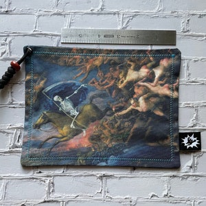 May include: A small, blue pouch with a drawstring closure. The pouch features a colourful image of a skeleton riding a horse, surrounded by angels and demons. The pouch has a small, black tag with a white logo.