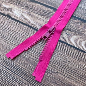 Può includere: Una cerniera lampo rosa con un cursore in metallo. La cerniera lampo è aperta e il cursore è al centro della cerniera lampo.